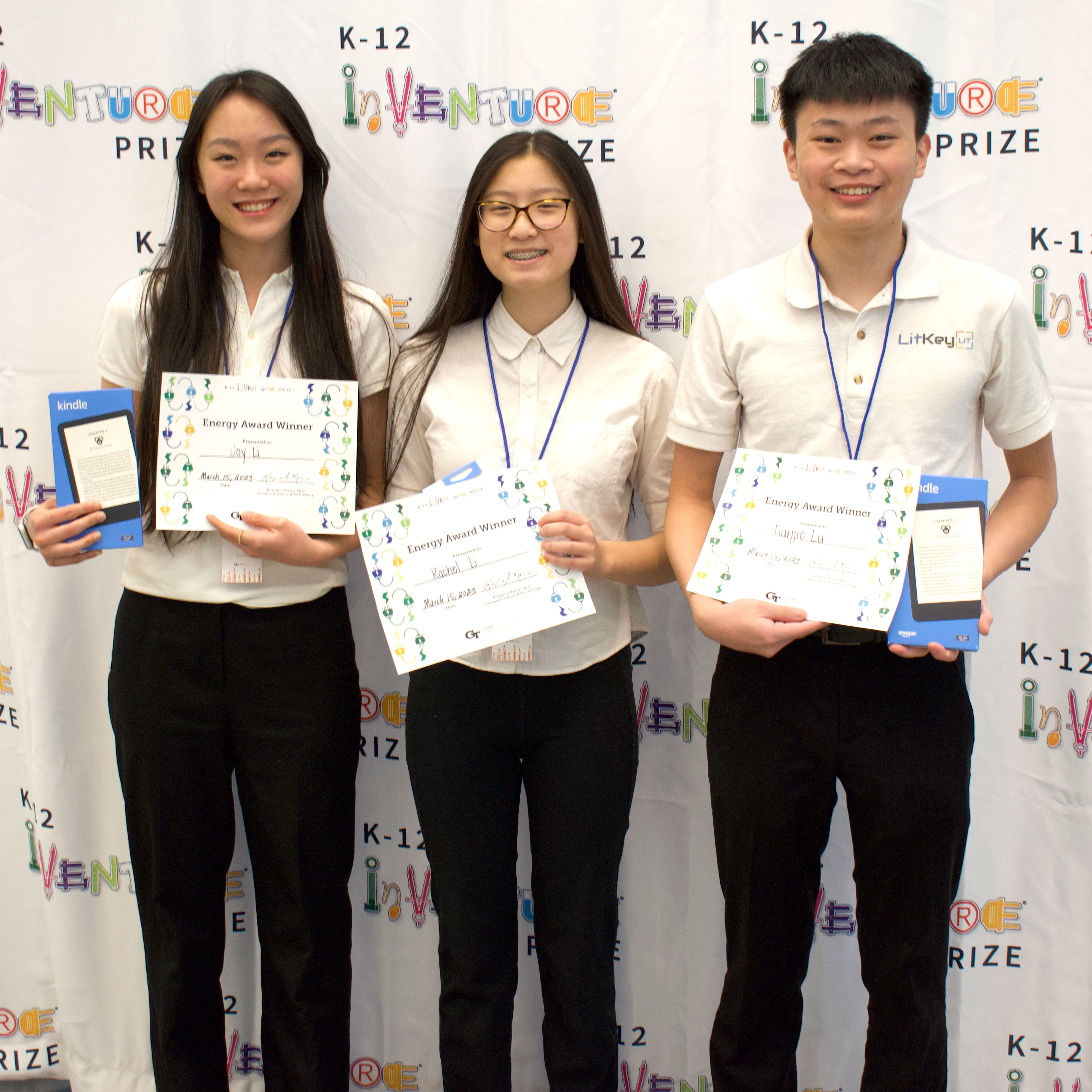 Three smiling students holding certificates and prizes (Kindles)