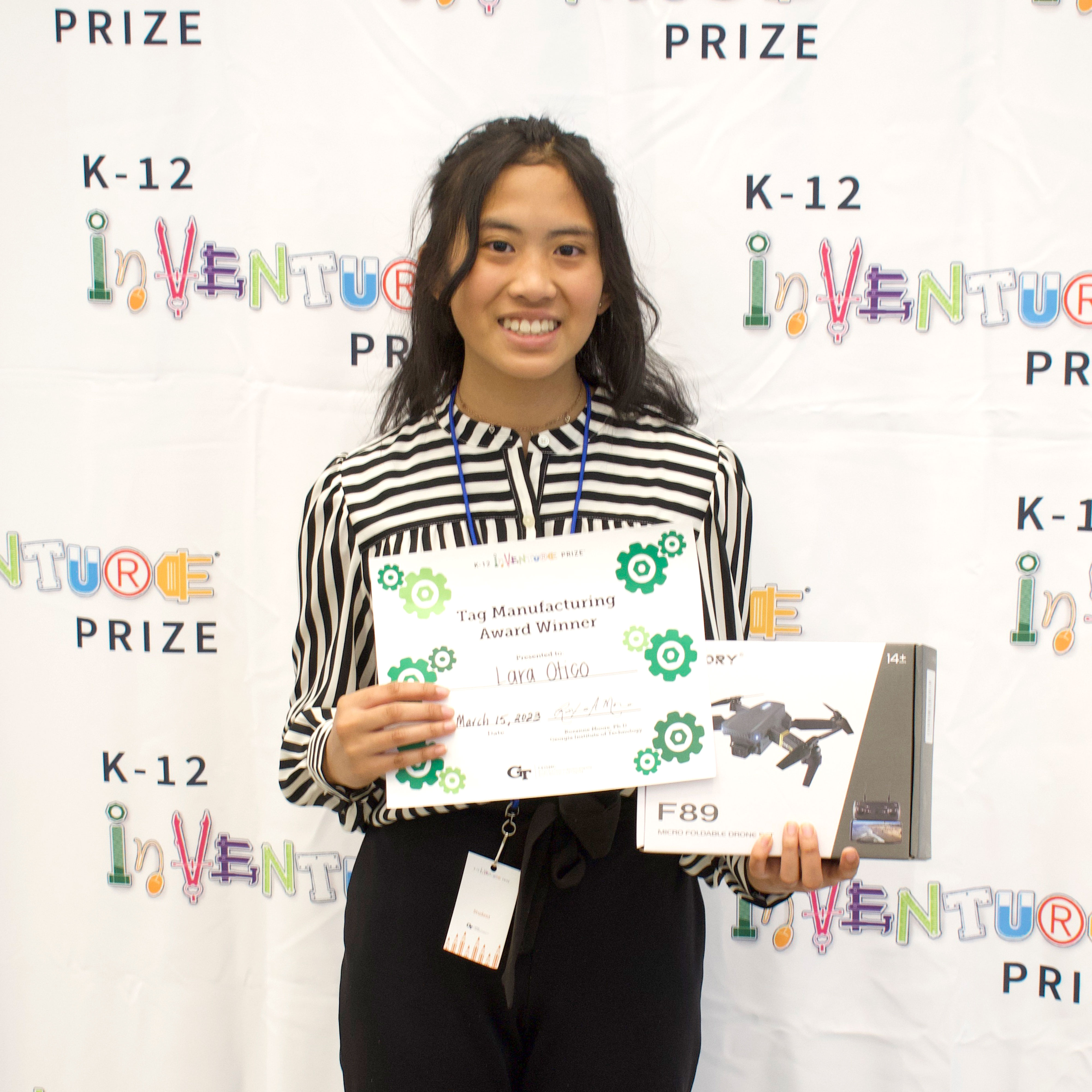 A smiling student holding up a certificate and a prize (drone)