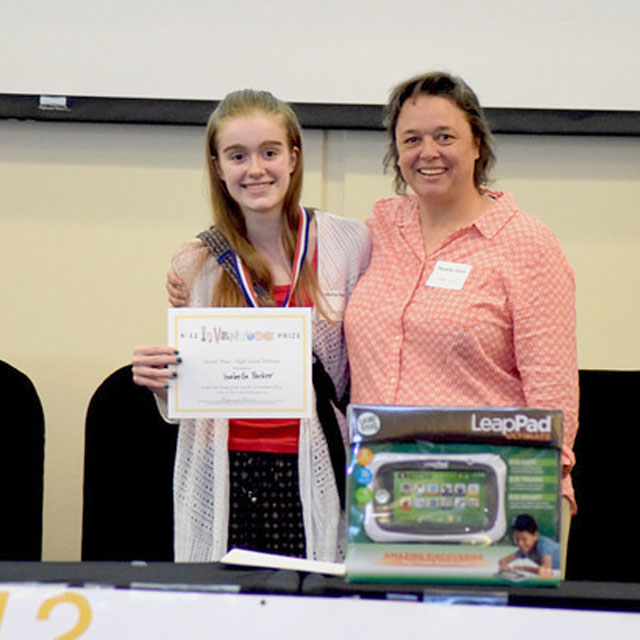 A smiling student holding up a certificate and standing beside a smiling adult