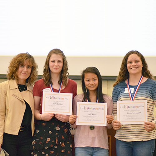Three smiling students holding up certificates and standing beside a smiling adult