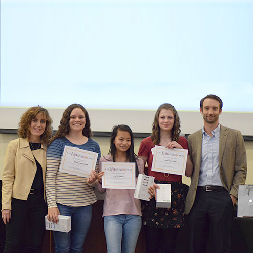 Three smiling students holding up certificates and standing beside two smiling adults
