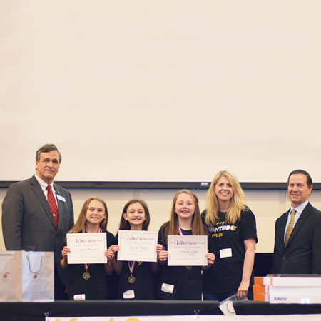 Three smiling students holding up certificates and standing beside three smiling adults