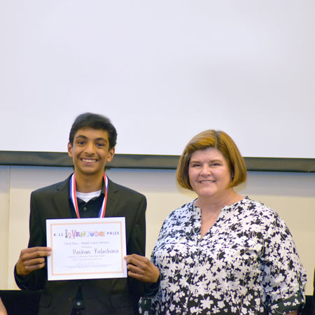 A smiling student holding up a certificate and standing beside a smiling teacher
