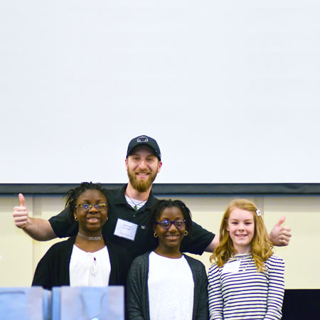 Three smiling students standing in front of a smiling adult
