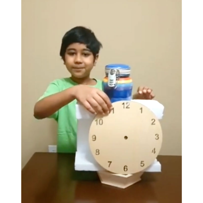 A smiling student showing an invention with a clock face cut out