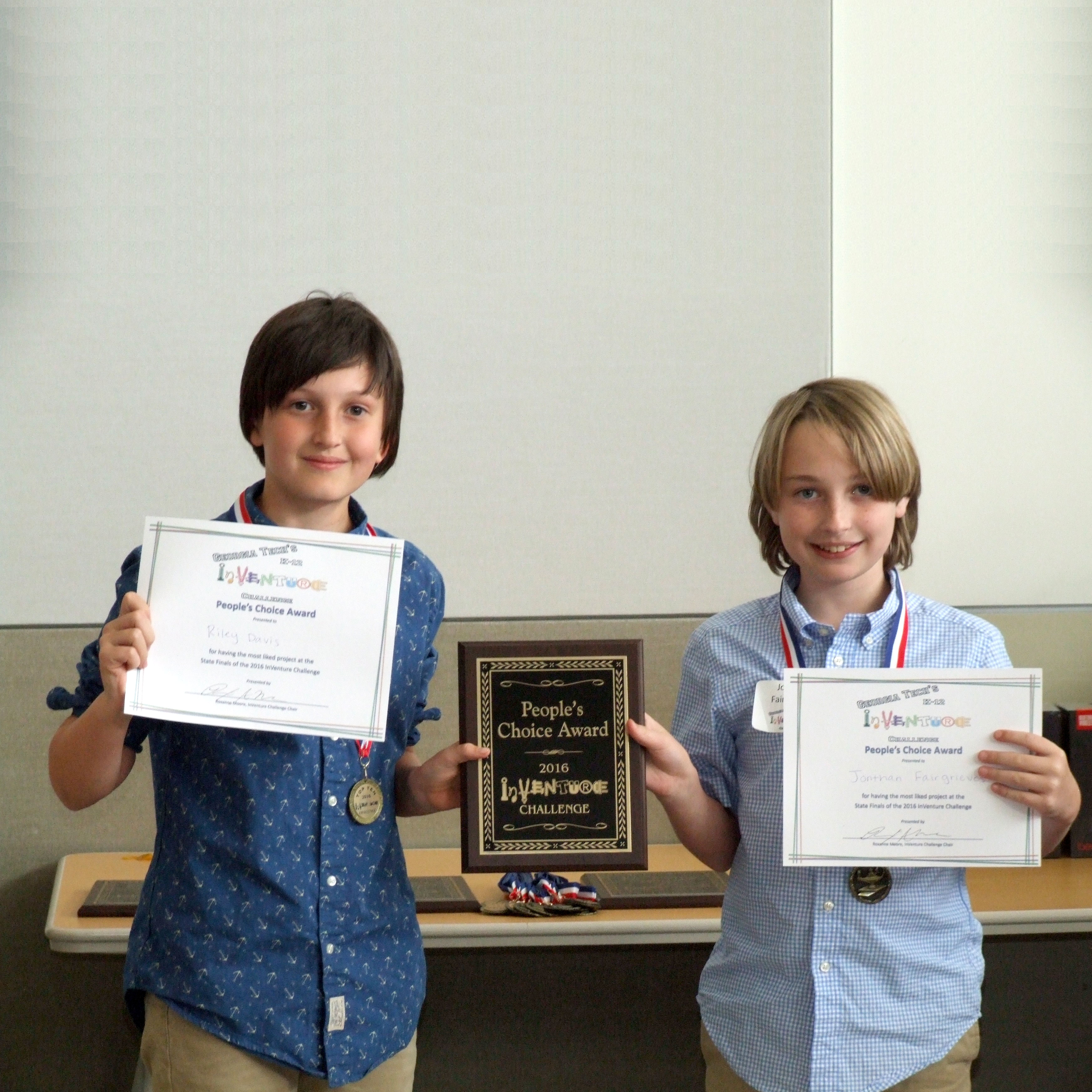 Two smiling students holding up certificates and a plaque