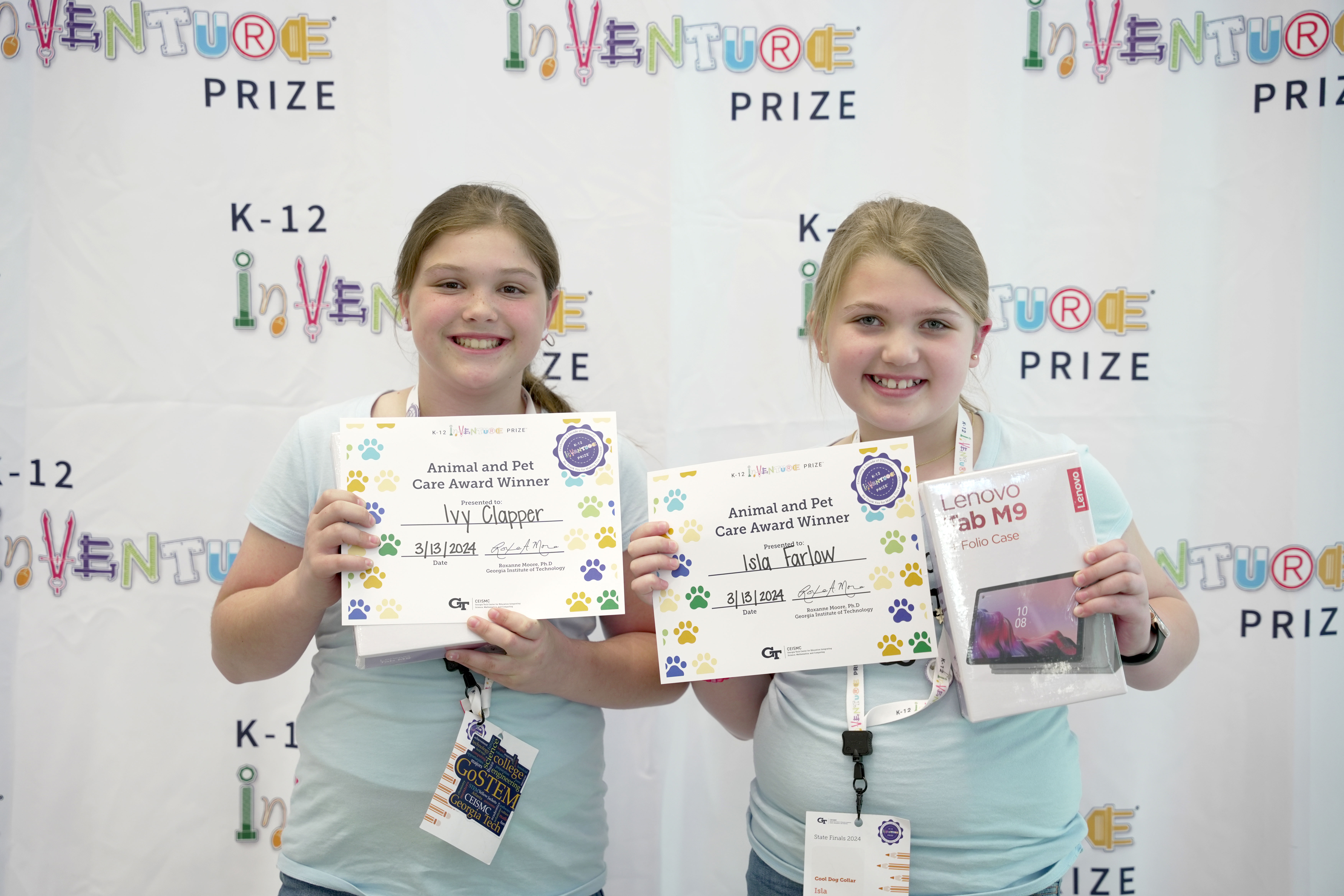 Two smiling students holding certificates and prizes