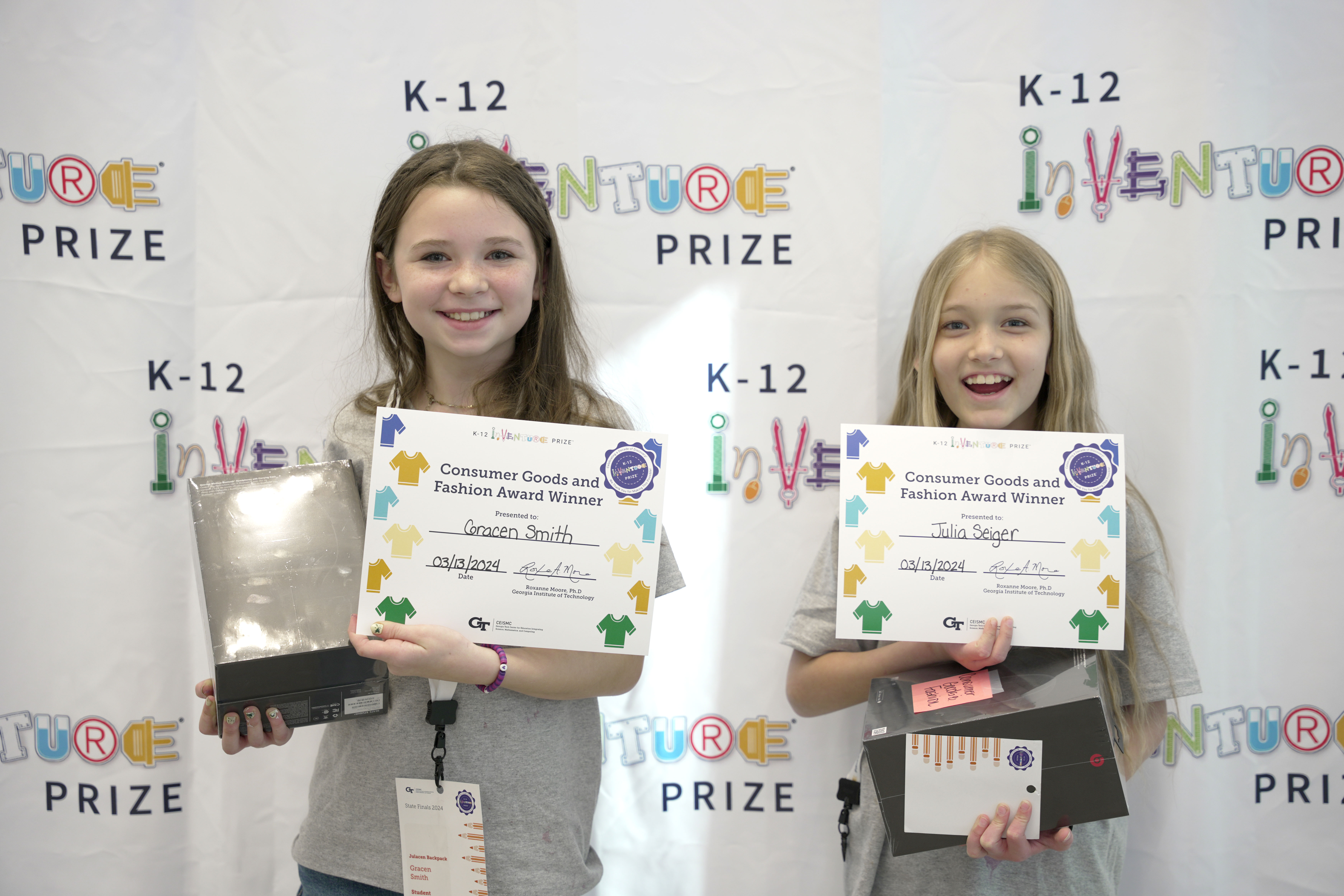 Two smiling students holding prizes and certificates