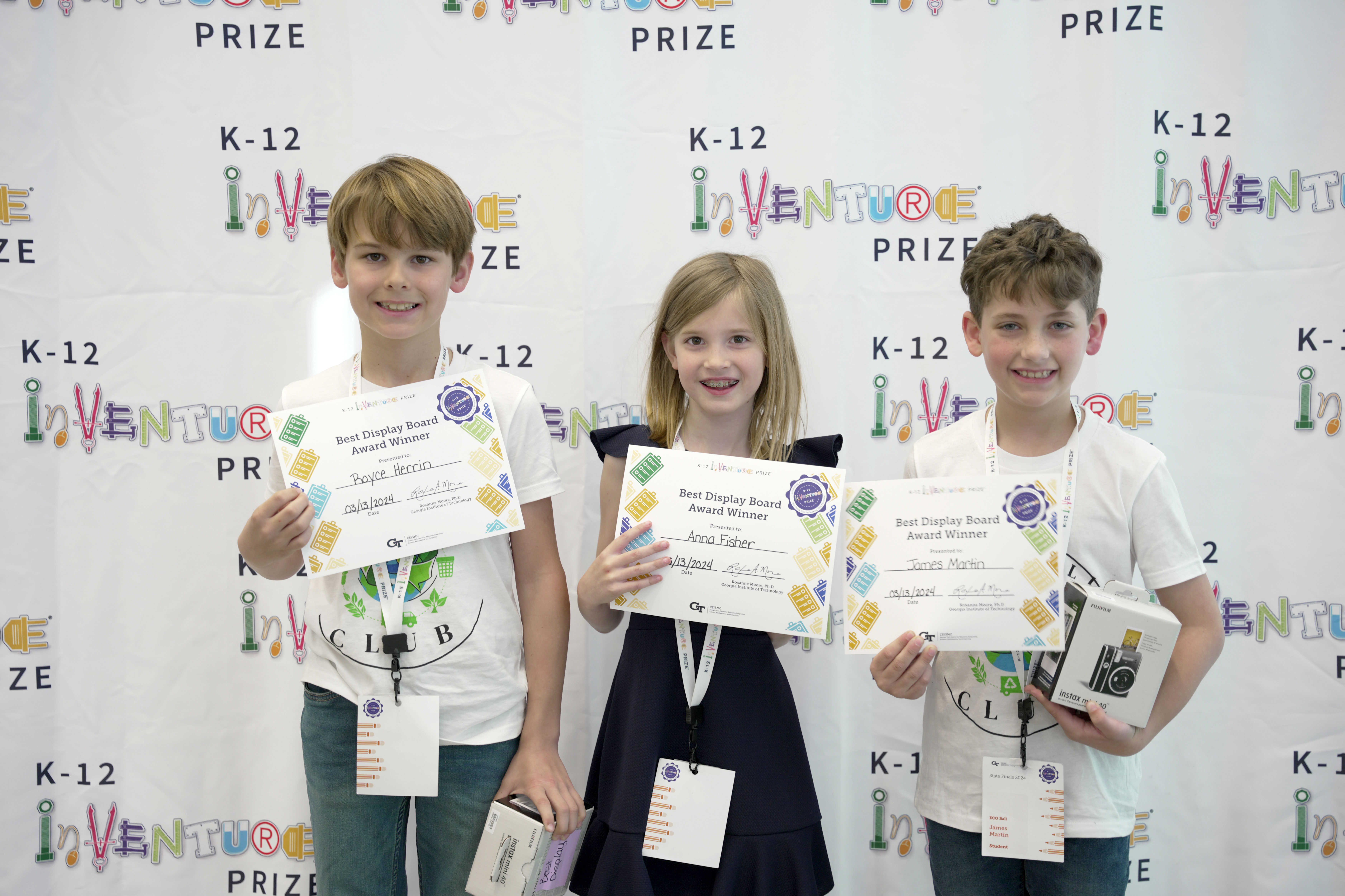 Three smiling students holding certificates and prizes
