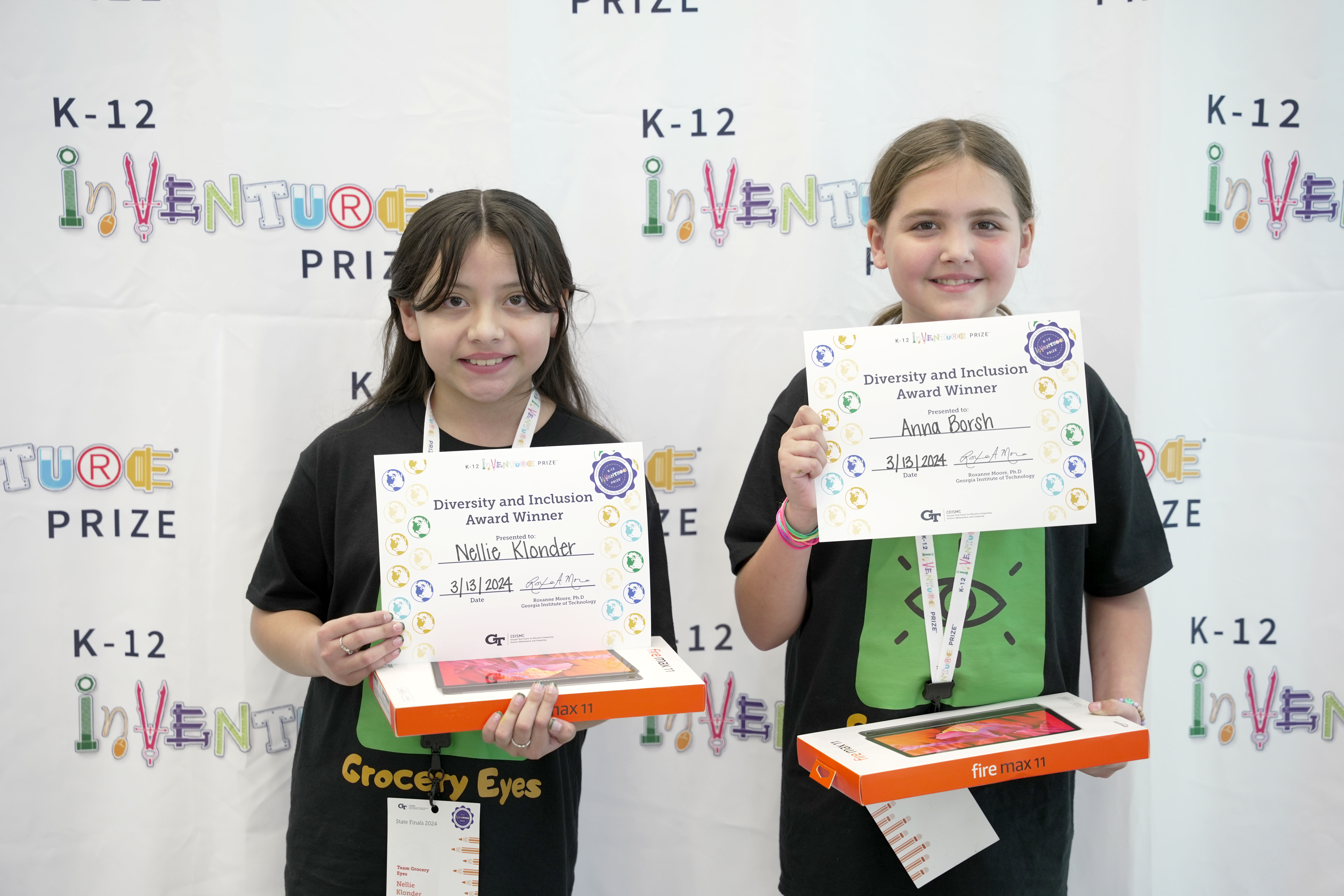 Two smiling students holding certificates and prizes