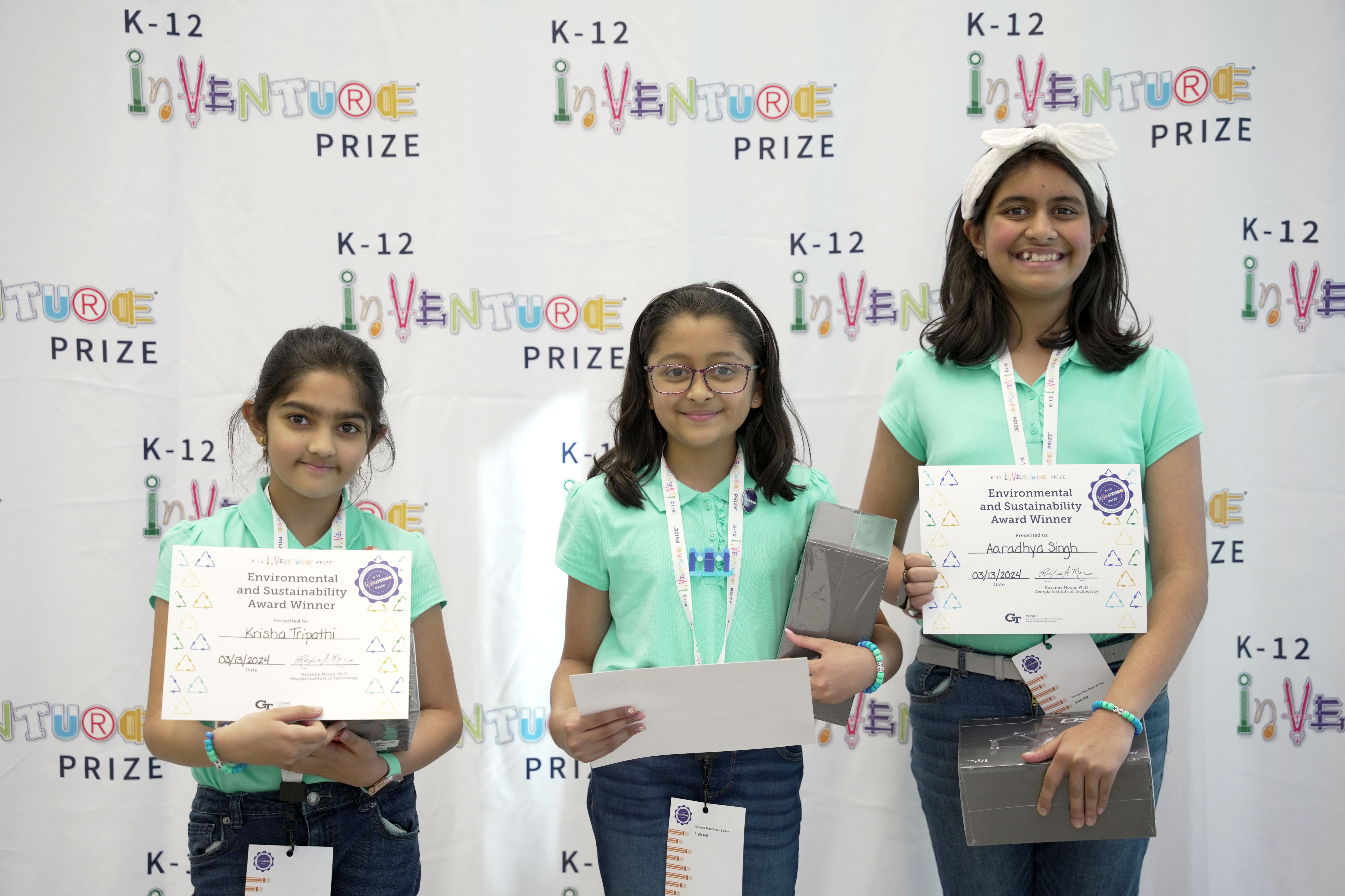 Three smiling students holding certificates and prizes