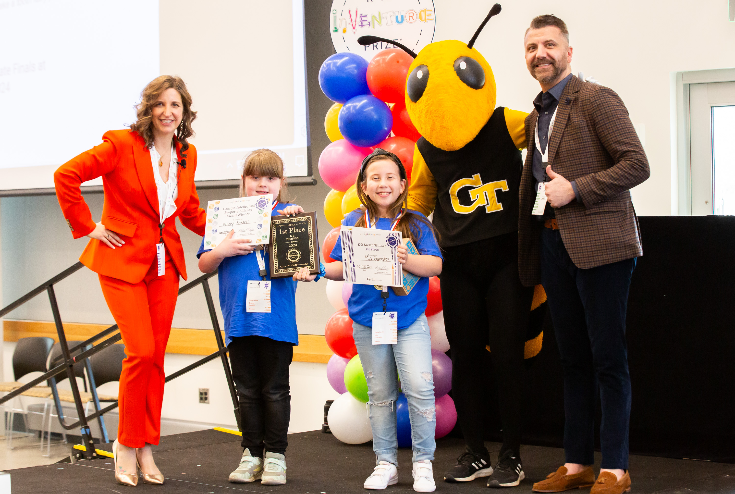 Two smiling adults standing with two smiling students and Buzz, the Georgia Tech yellowjacket mascot