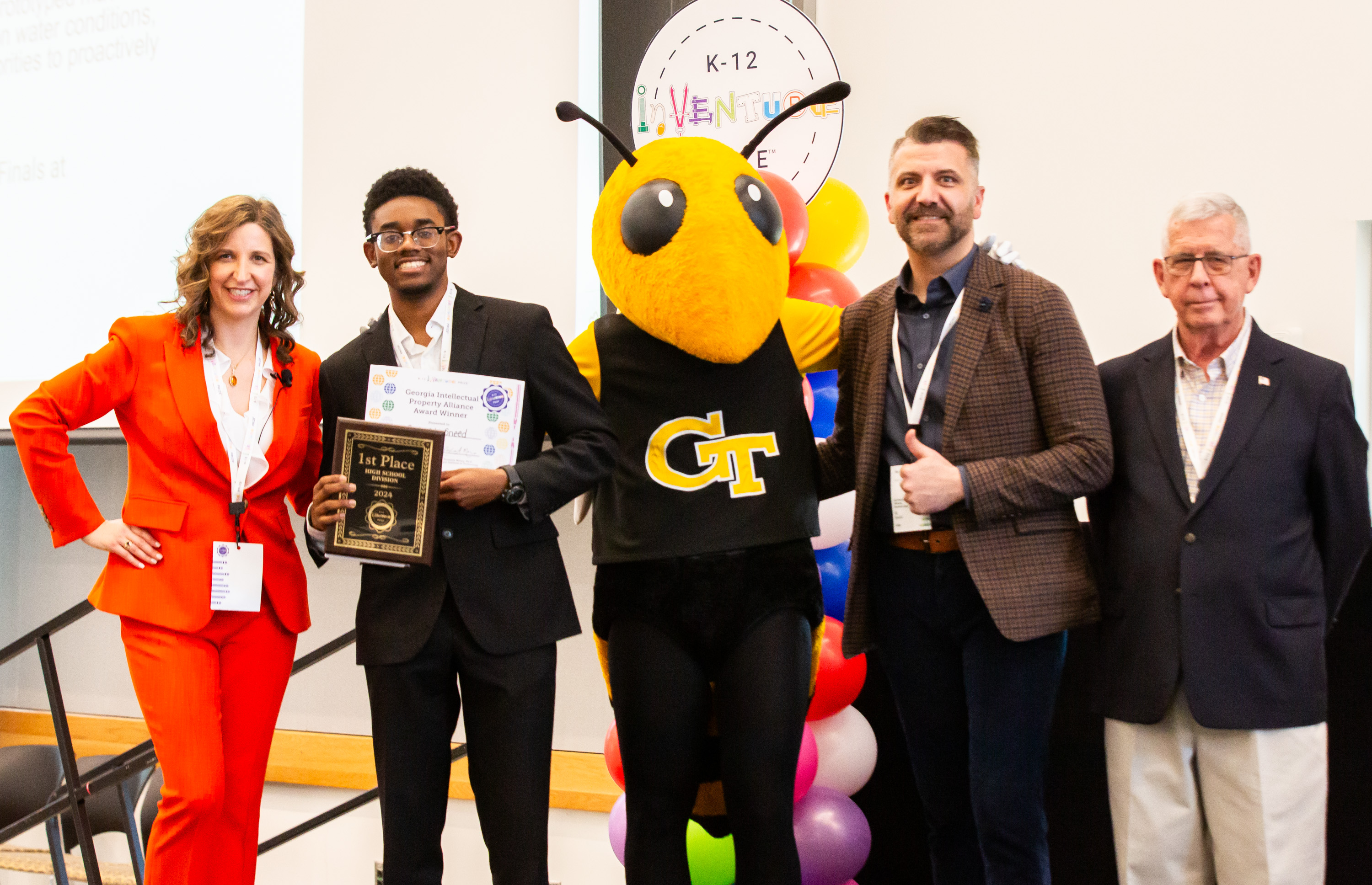 Three smiling adults standing with a smiling student holding a certificate and plaque and Buzz, the Georgia Tech yellowjacket mascot