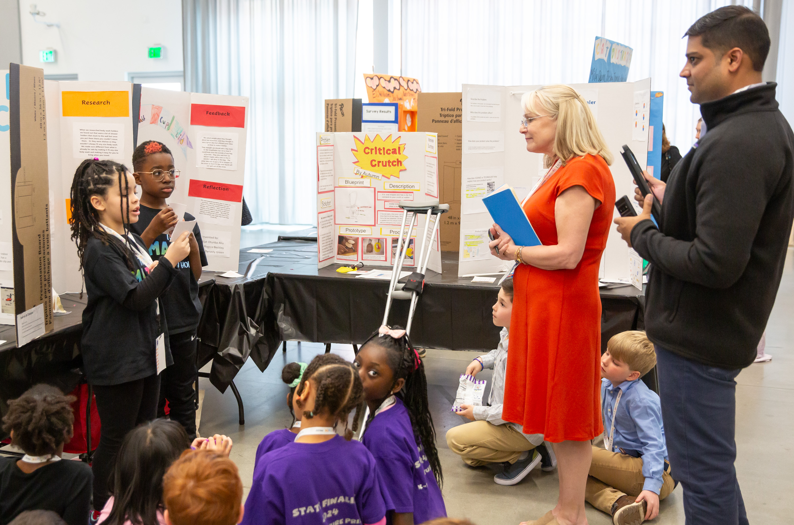 Two adults judging a group of students and their poster