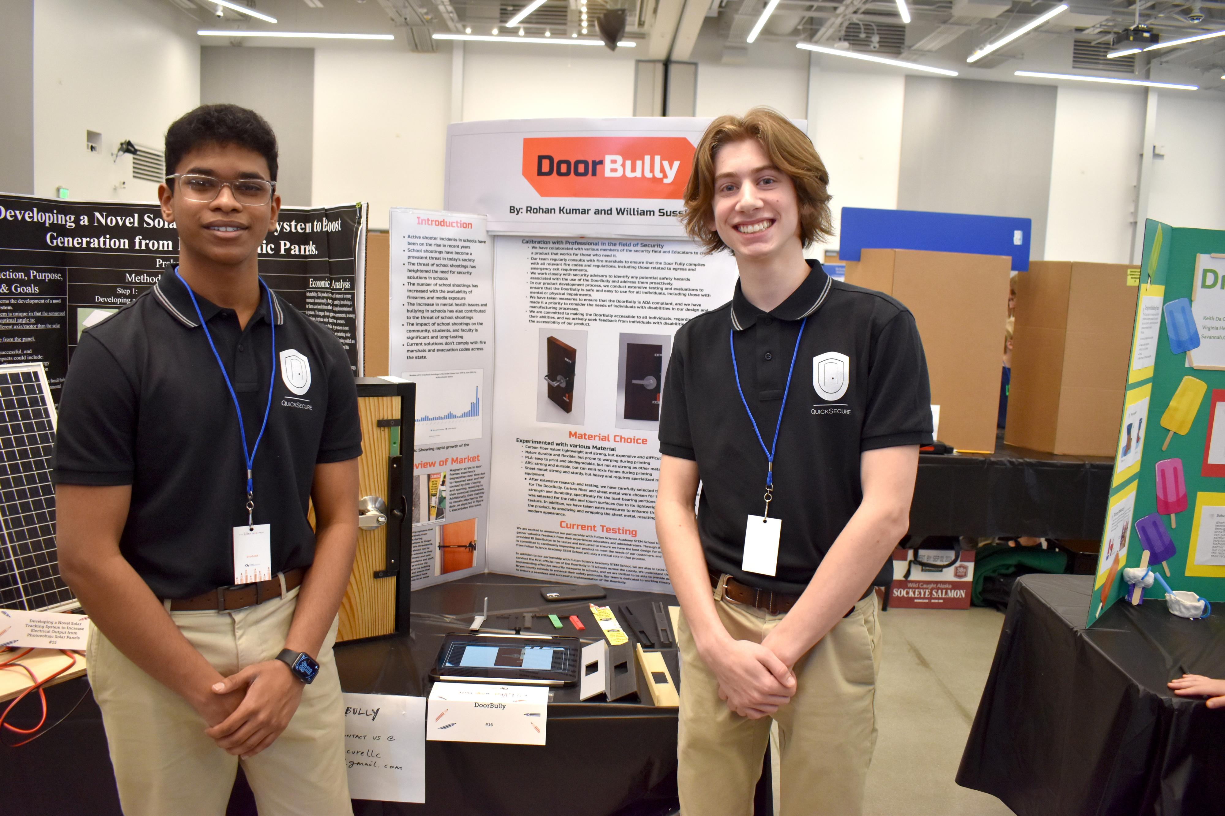 Two students standing in front of a poster and a prototype