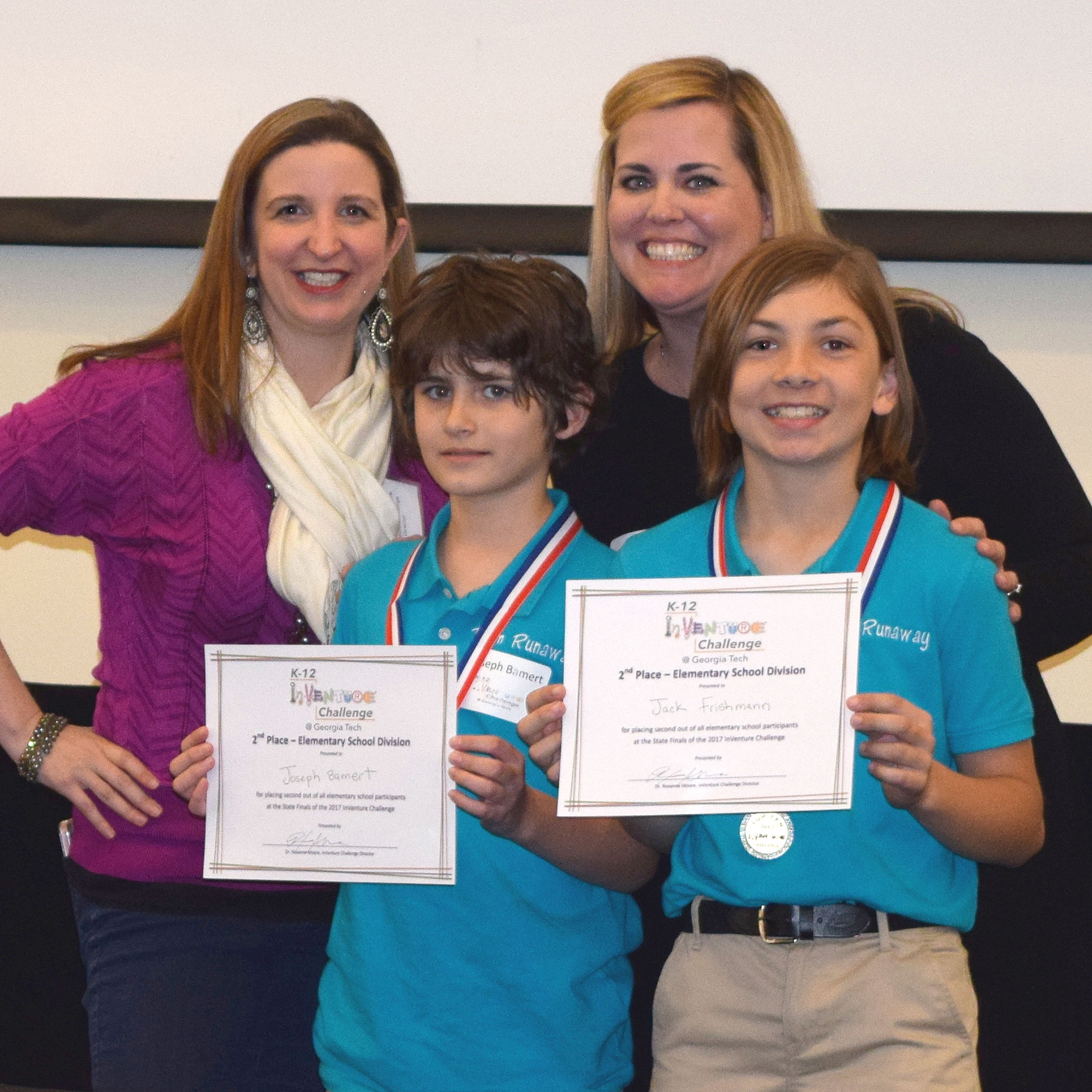 Two smiling students holding up certificates and standing in front of two smiling adults