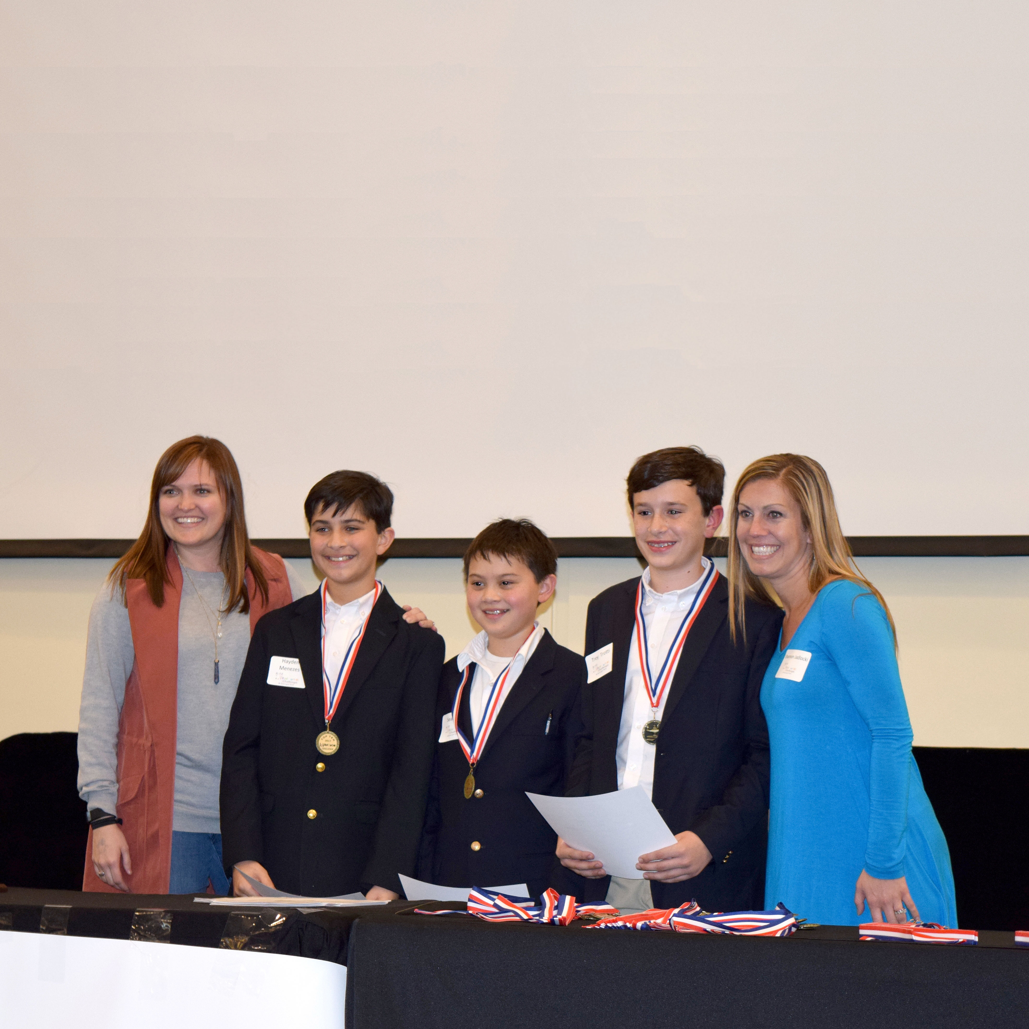 Three smiling students standing next to two smiling adults