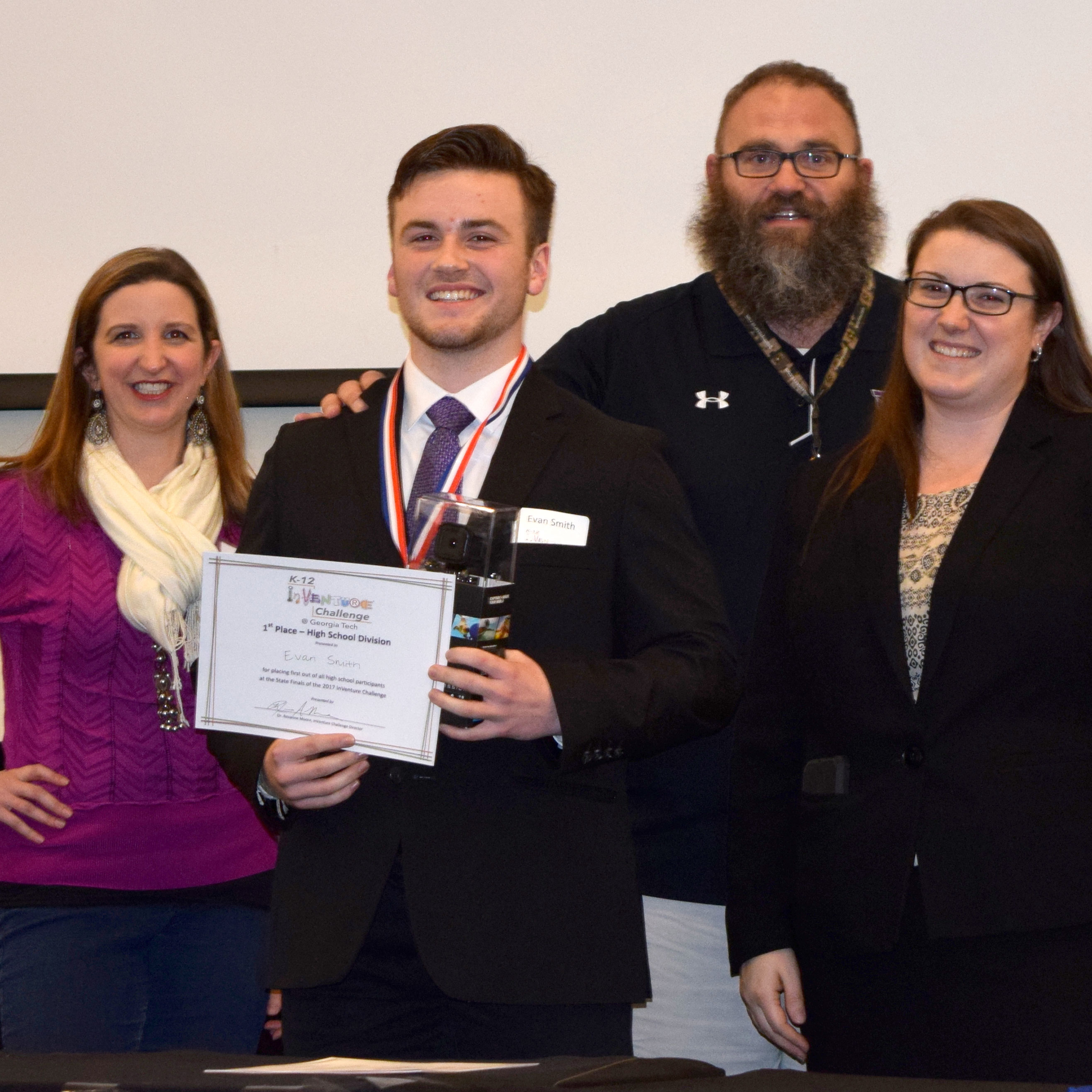 A smiling student holding up a certificate and standing next to three smiling adults