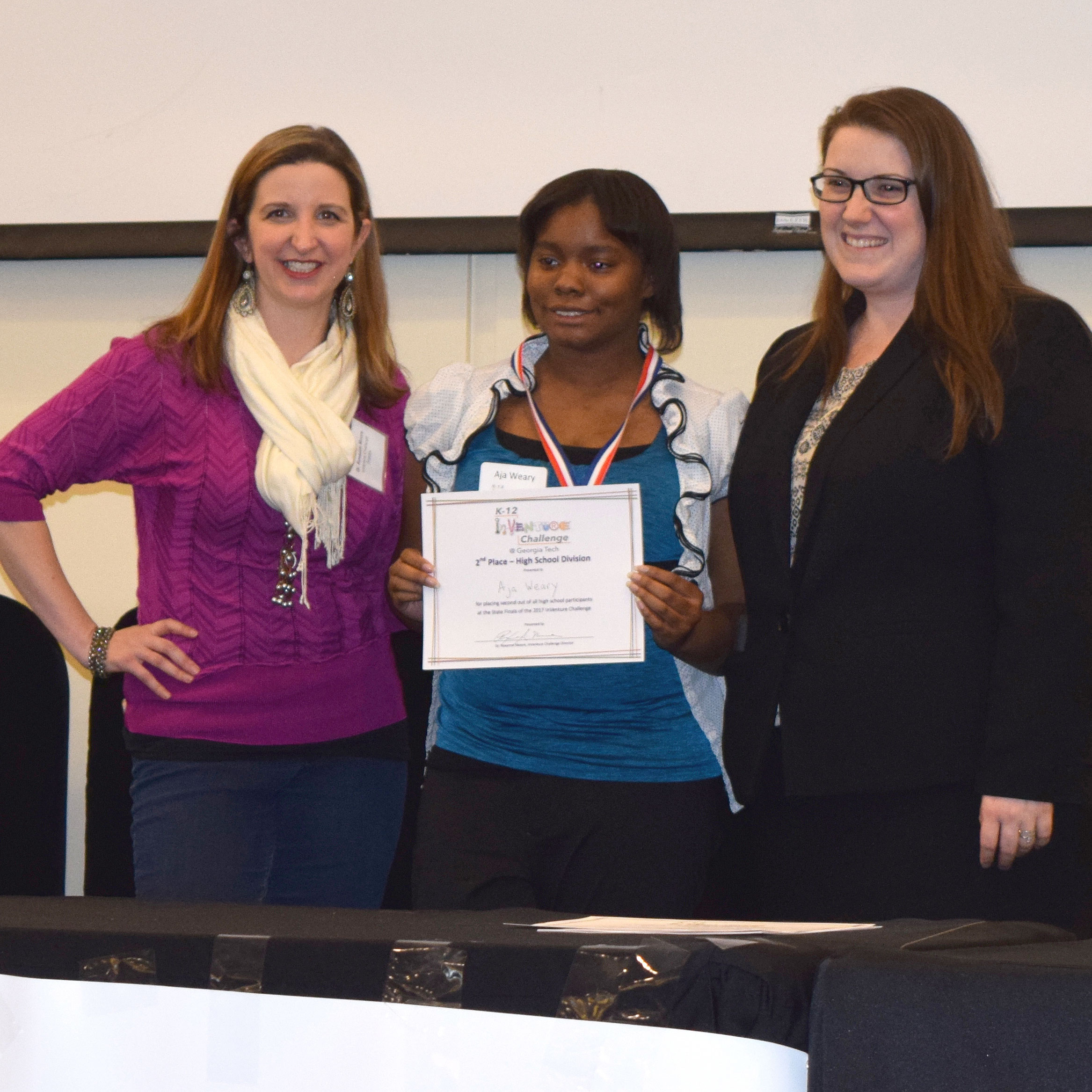 A smiling student holding up a certificate and standing next to two smiling adults